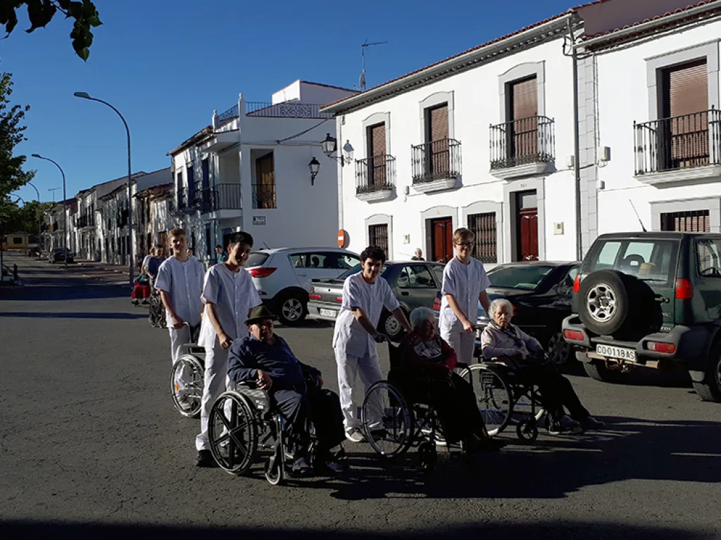 Eine Gruppe schiebt Rollstühle durch eine Straße mit weißen Häusern.